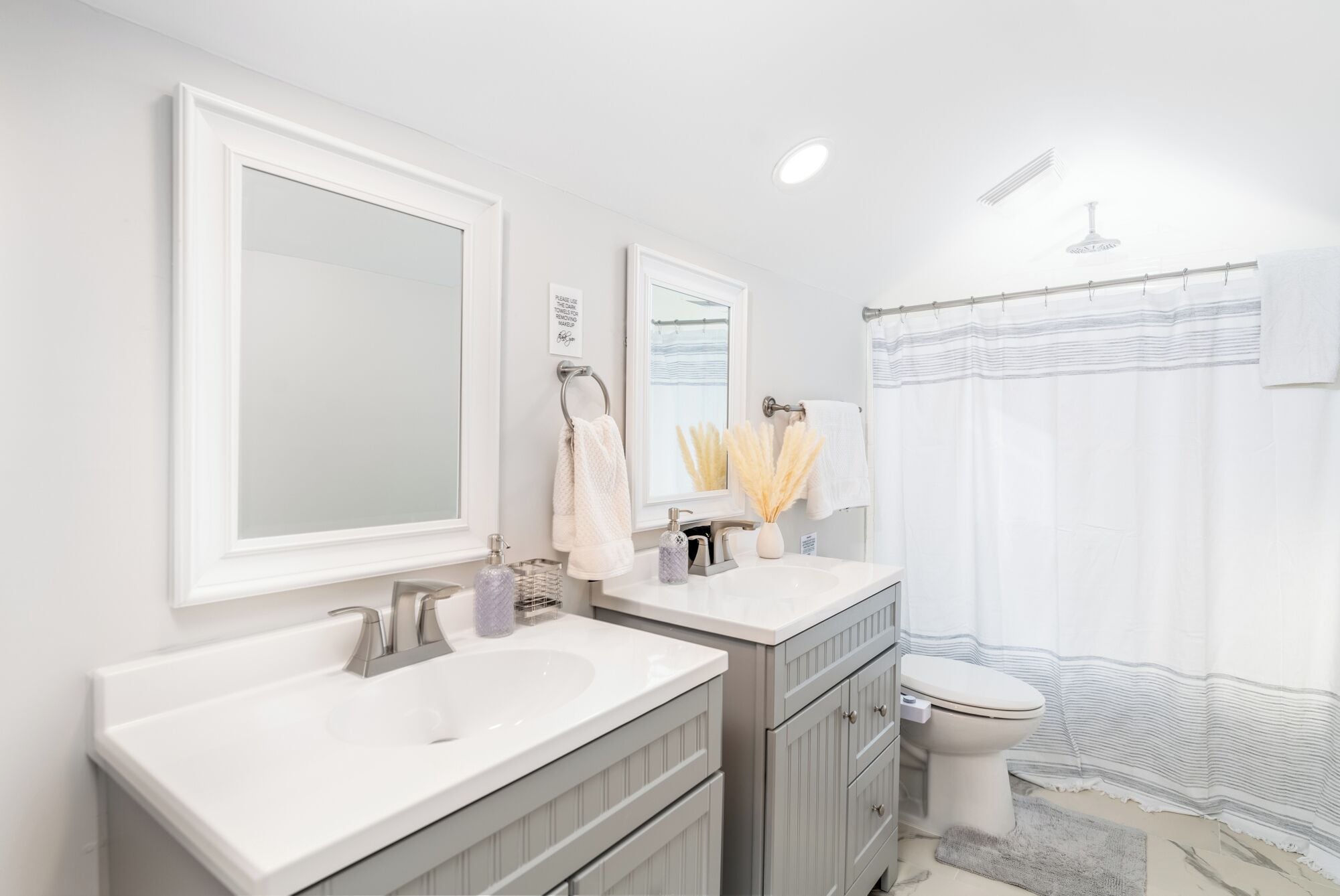 A modern bathroom with a double sink vanity, a toilet, and a shower curtain.