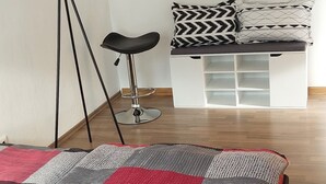 A modern bedroom with a large bed, a floor lamp, a bench with patterned cushions, and a cityscape view. - Vacation apartment "Mittags-Ruh" in the center of Reichenbach/Vogtland. (Reichenbach im Vogtland)