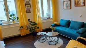 A living room with a blue sofa, two round tables, yellow curtains, and potted plants. - Vacation apartment "Mittags-Ruh" in the center of Reichenbach/Vogtland. (Reichenbach im Vogtland)