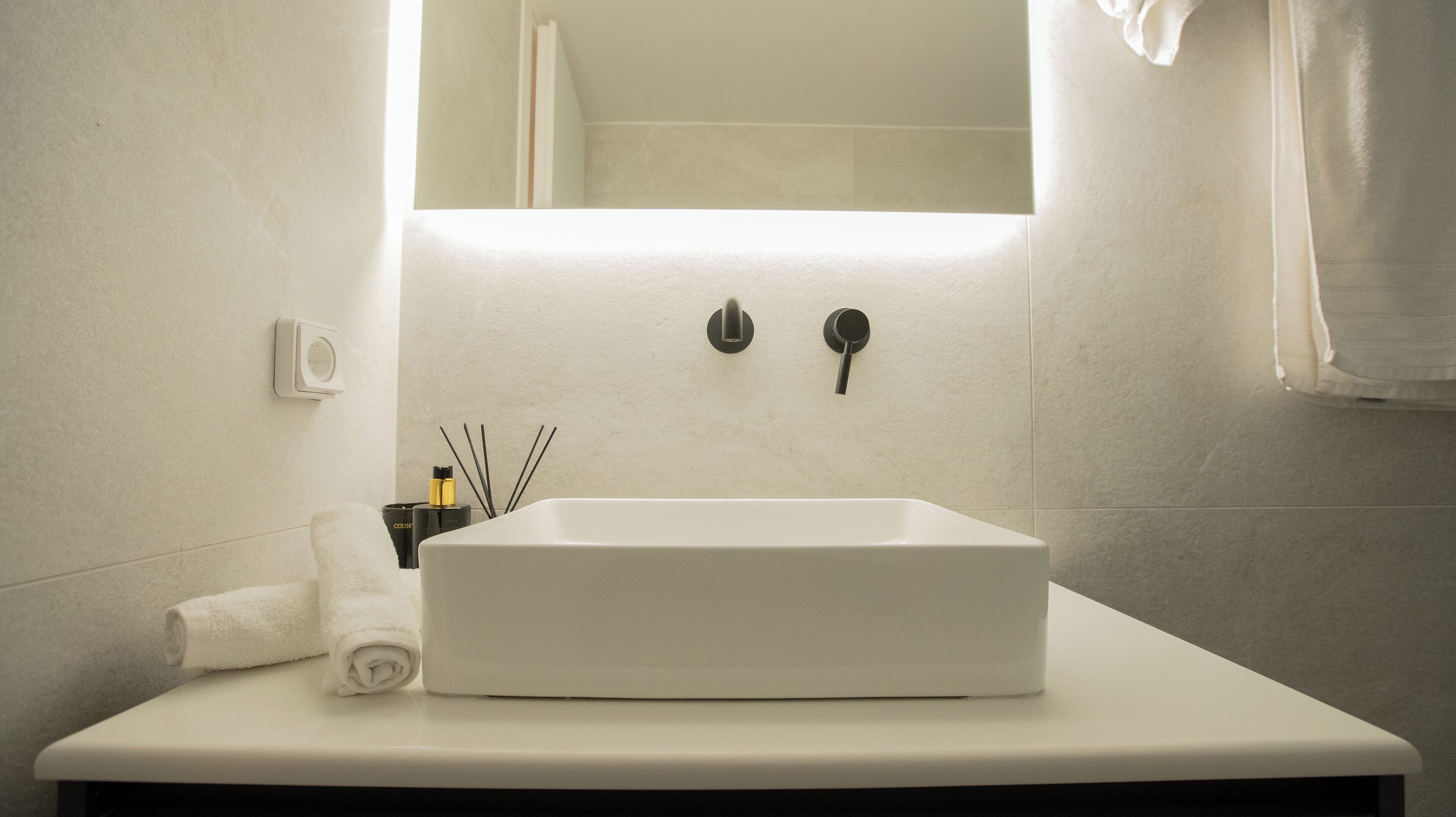 Een witte badkamer met een rechthoekig wastafelmeubel, een spiegel erboven en een handdoek op het aanrecht.