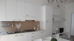 A modern kitchen with white cabinets, a gas stove, a sink, and a dining area with a table and chairs. - Peschierahome - Arilica (Peschiera del Garda)