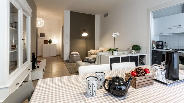 A modern kitchen with white cabinets, a dining table with a checkered tablecloth, and a coffee station. - Il Mincio - Peschierahome (Peschiera del Garda)