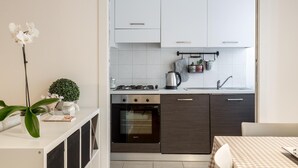 A modern kitchen with white cabinets, a built-in oven, and a dining area with a checkered tablecloth. - Il Mincio - Peschierahome (Peschiera del Garda)