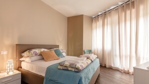 A neatly made bed with a blue bedspread, a bedside table with a lamp, and a window with curtains. - La Rocca - Peschierahome (Peschiera del Garda)