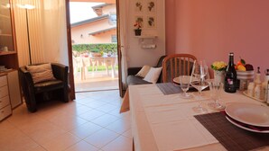 Un coin repas avec une table dressée pour deux personnes, une chaise, un canapé et une vue sur l’extérieur.