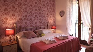 Une chambre à coucher avec un papier peint à motifs floraux, un lit avec une literie rouge, deux lampes de chevet et une fenêtre avec des rideaux.