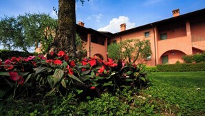 A building with a red facade, a large tree, and a garden with red flowers. - Bellasirmione - Le Vele (Sirmione)