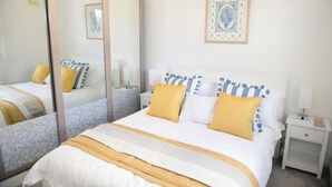 Un dormitorio ordenado con una cama grande, mesitas de noche, un espejo y una obra de arte enmarcada en la pared.