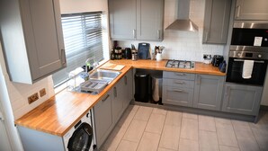 Cocina moderna con armarios grises, encimera de madera, electrodomésticos de acero inoxidable y lavadora integrada.