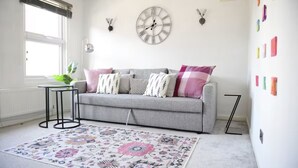 Una sala acogedora con un sofá gris, un tapete estampado y un reloj de pared.