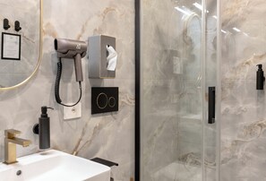 Une salle de bain moderne avec un mur en marbre, un sèche-cheveux, un distributeur de serviettes et une cabine de douche en verre.