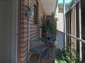 Un petit patio extérieur avec un mur en briques, une terrasse en bois, une table ronde avec deux chaises et des plantes en pot.