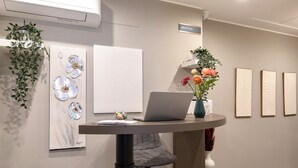 Un espace d’accueil avec un ordinateur portable posé sur une table ronde, un tableau blanc et des œuvres d’art encadrées accrochées au mur.