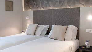 Une chambre d’hôtel avec deux lits, un mur à texture, une tête de lit moderne, des lampes de chevet et une petite table avec une bouteille.