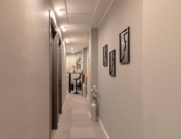 A hallway with a modern design, featuring a long corridor, a dining area in the background, and three abstract wall art pieces. - AH - Duomo Signature (Milan)