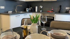Et moderne køkken med hvide skabe, en sort bordplade og en spiseplads med et bord dækket til to.