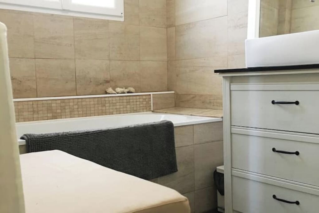 A bathroom with a bathtub, a towel rack, and a white cabinet with drawers.