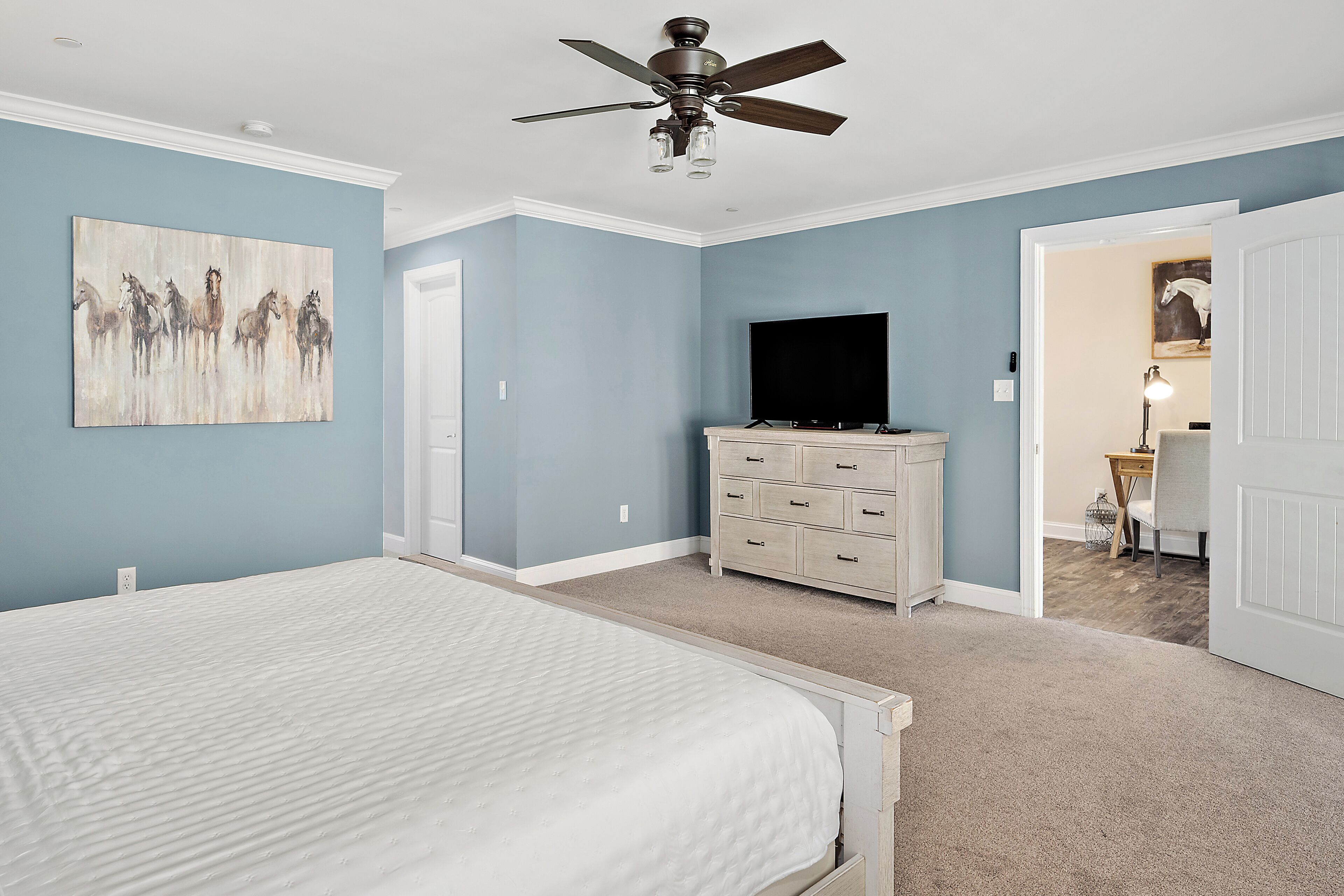 A bedroom with a bed, a dresser, a television, and a ceiling fan.