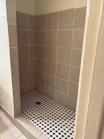 A shower with beige tiles and a black and white checkered floor.
