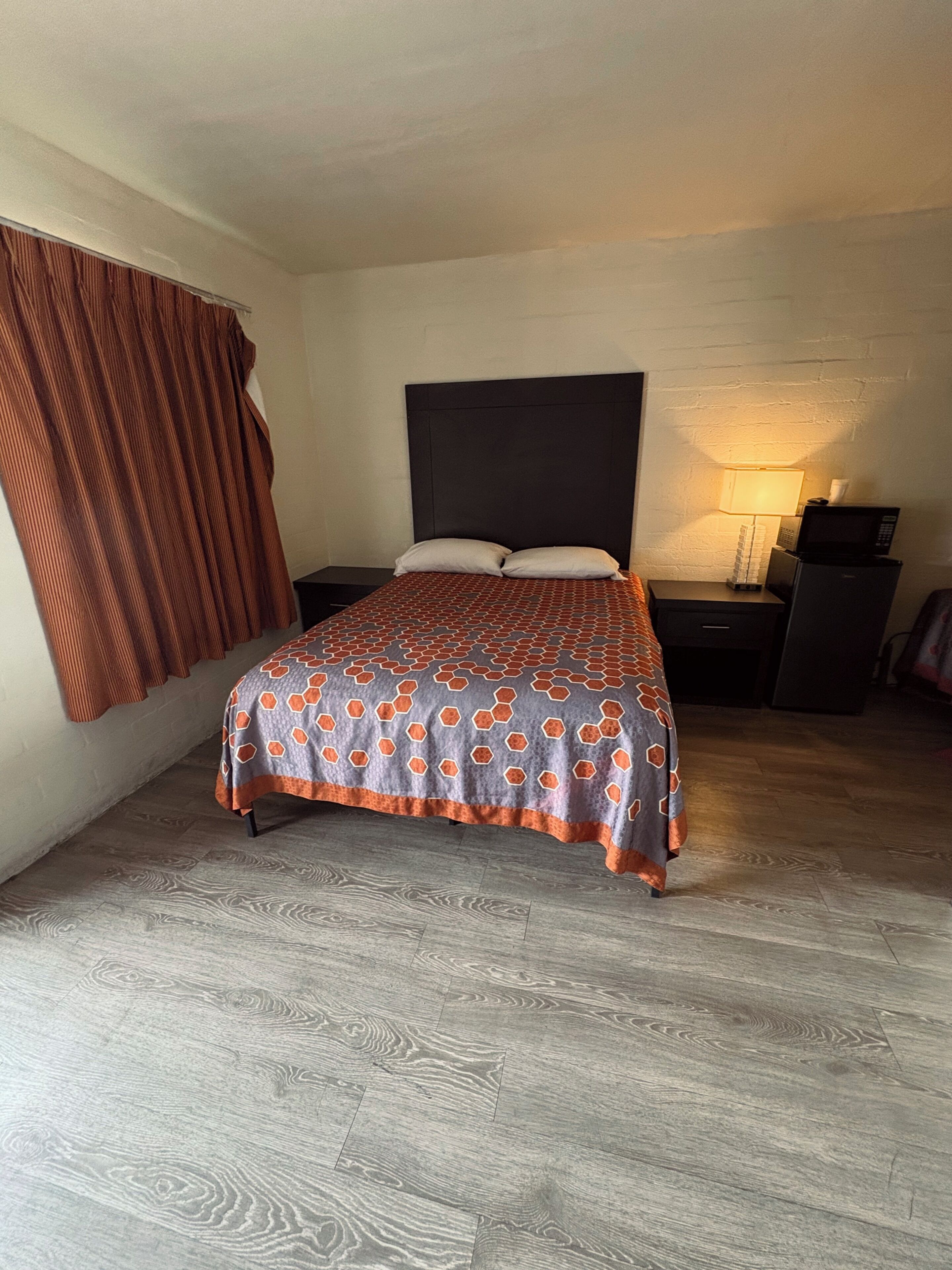 A bedroom with a bed, a nightstand, a lamp, and a microwave.