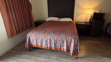 A bedroom with a bed, a nightstand, a lamp, and a microwave.