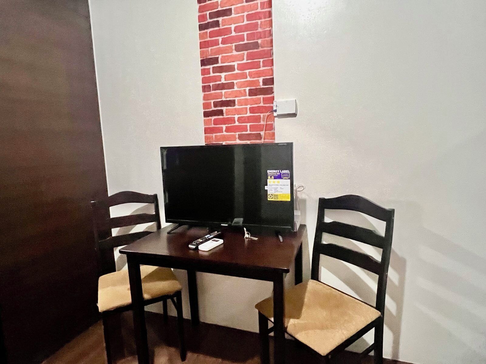 A small room with a TV on a wooden table, two chairs, and a brick wall.