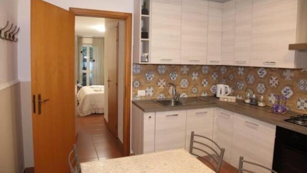 Een compacte keuken met witte kasten, een betegelde spatwand, en een eethoek met een tafel en stoelen.