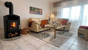 A living room with a wood-burning stove, a sofa, a coffee table, and a painting on the wall. - Apartment GoodTimes, ground floor, 2 x 50" TV, Netflix, south-facing terrace w. Access to the parking lot (Aarbergen)