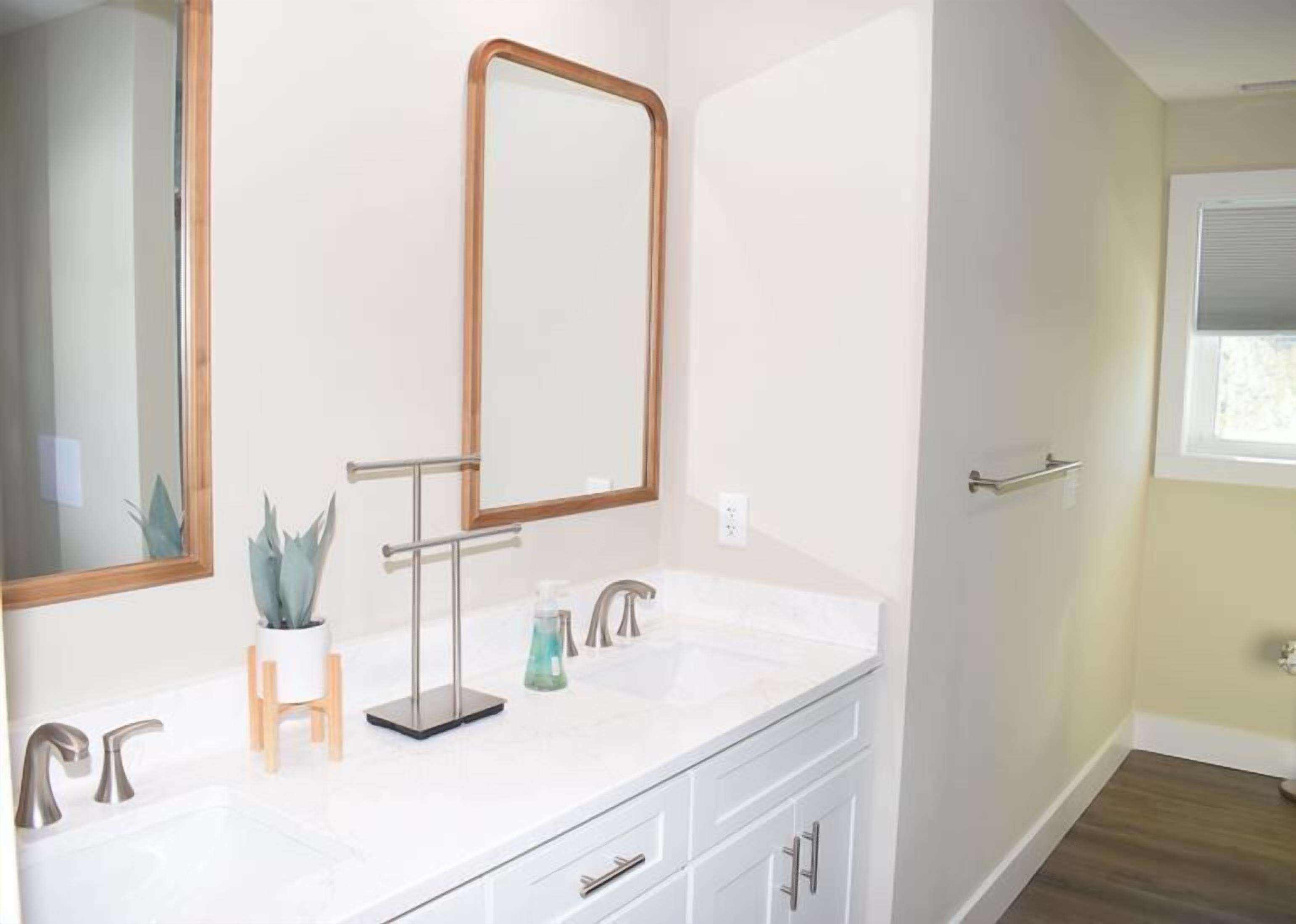 A bathroom with a white vanity, a large mirror, a potted plant, and a window.