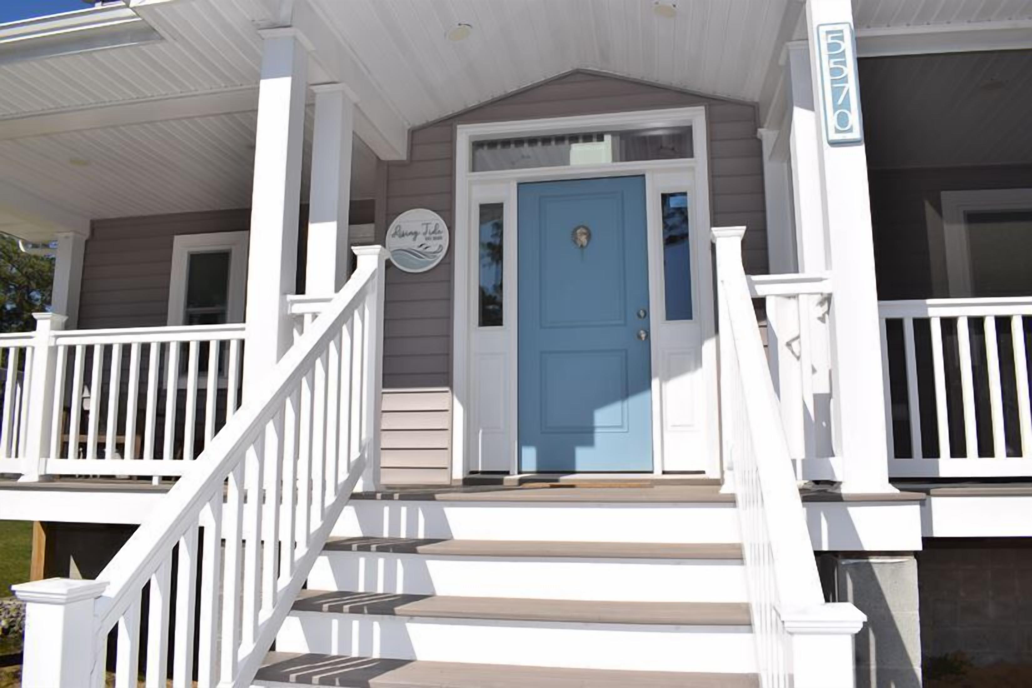 A house with a blue front door, white railings, and a porch with steps leading to the entrance.