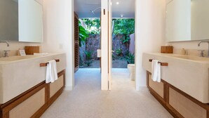 Een moderne badkamer met twee wastafels, een grote spiegel en uitzicht op een tuin door een open deur.