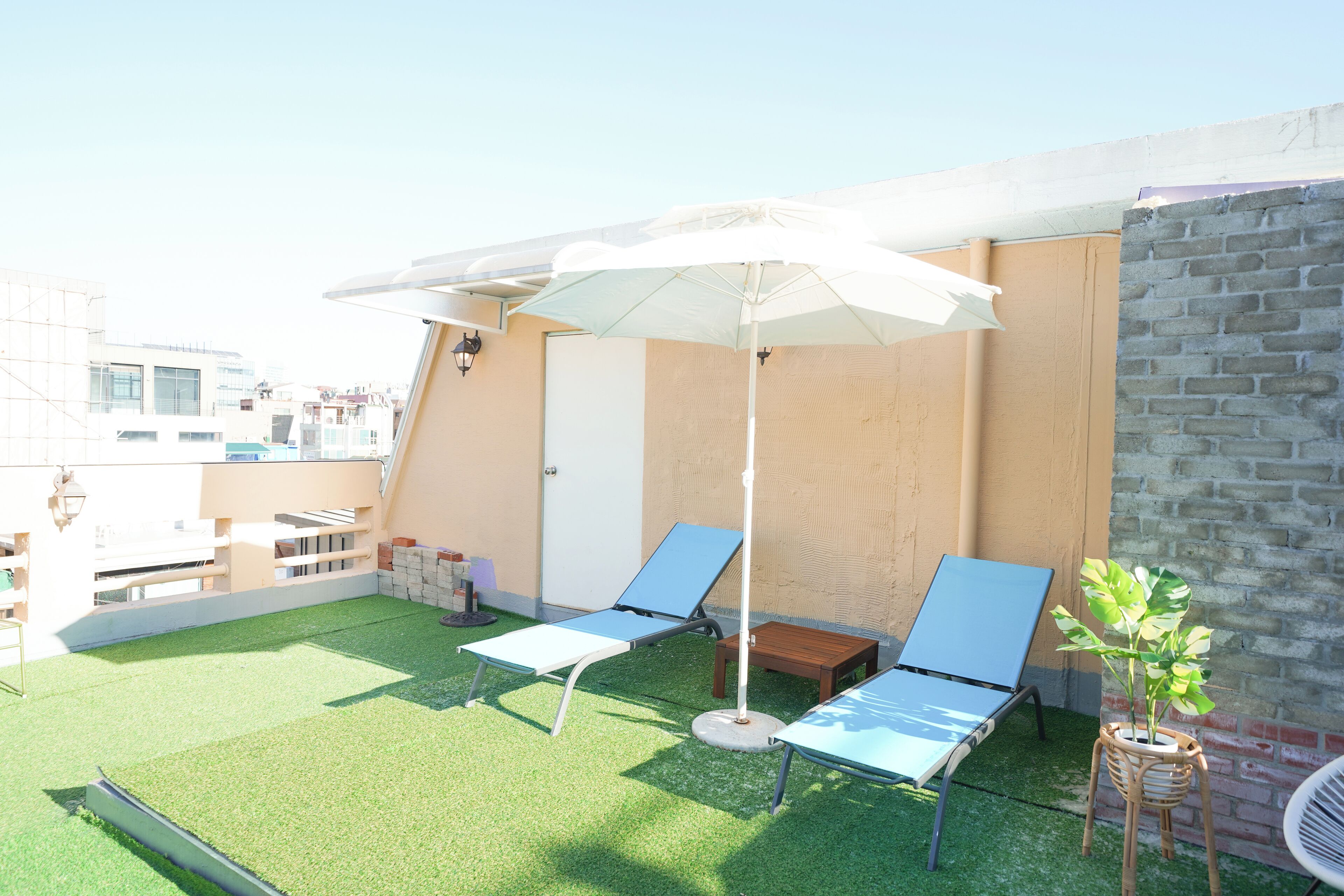 A rooftop terrace with two lounge chairs, a white umbrella, and a potted plant.
