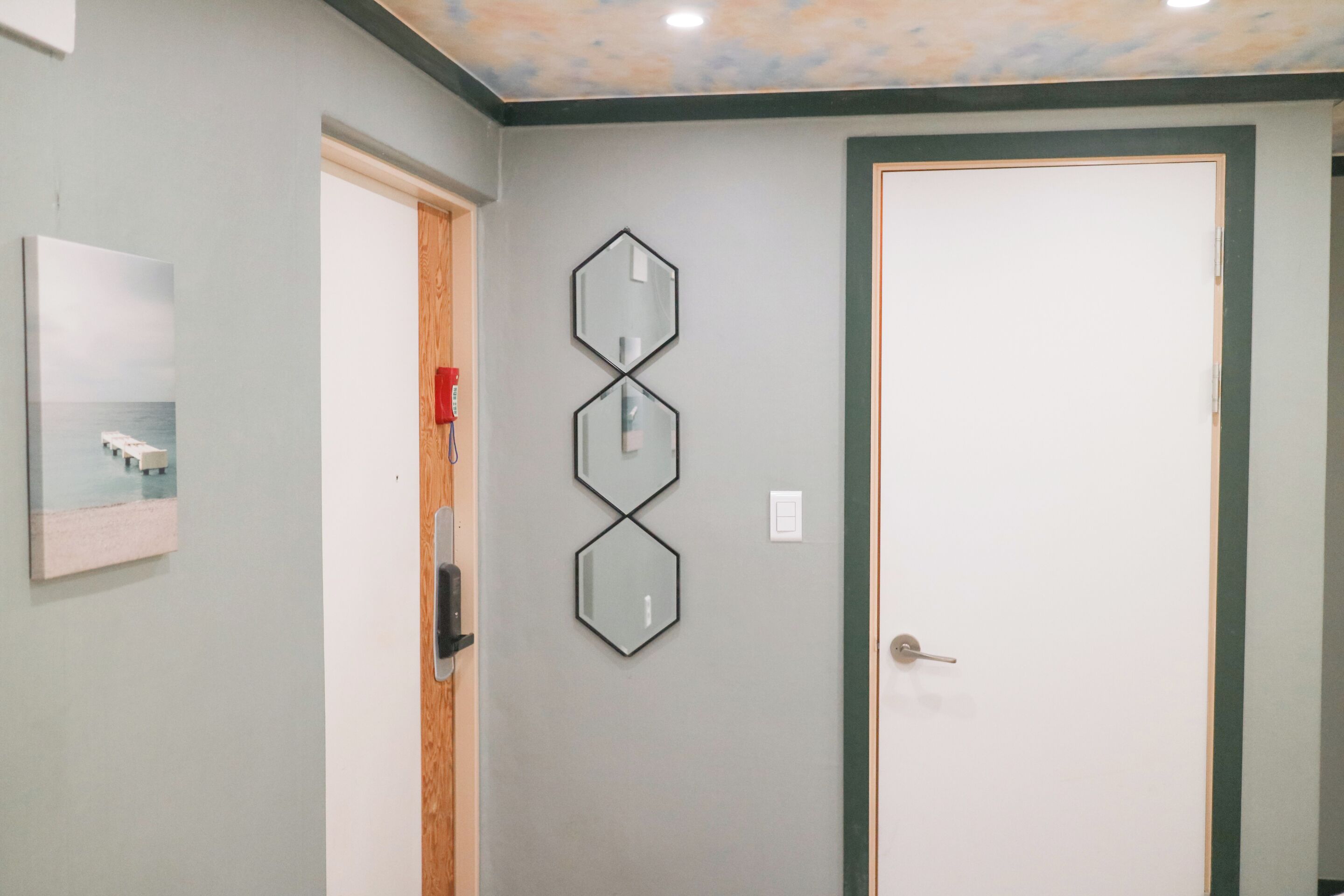 A bathroom with a white door, a mirror, and a wall-mounted light fixture.