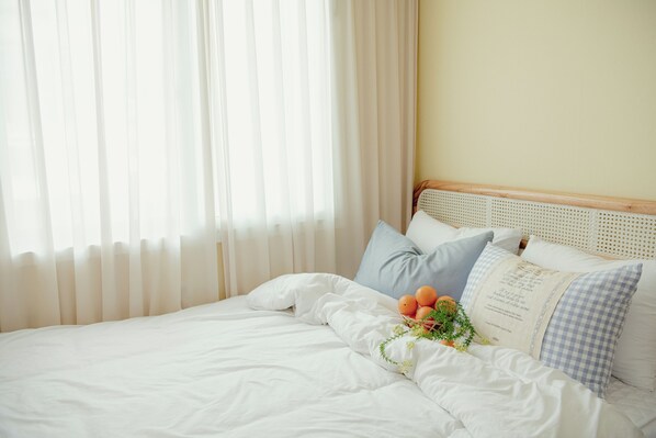 Una cama bien hecha con sábanas blancas, un cojín a cuadros y un pequeño arreglo de naranjas y follaje.