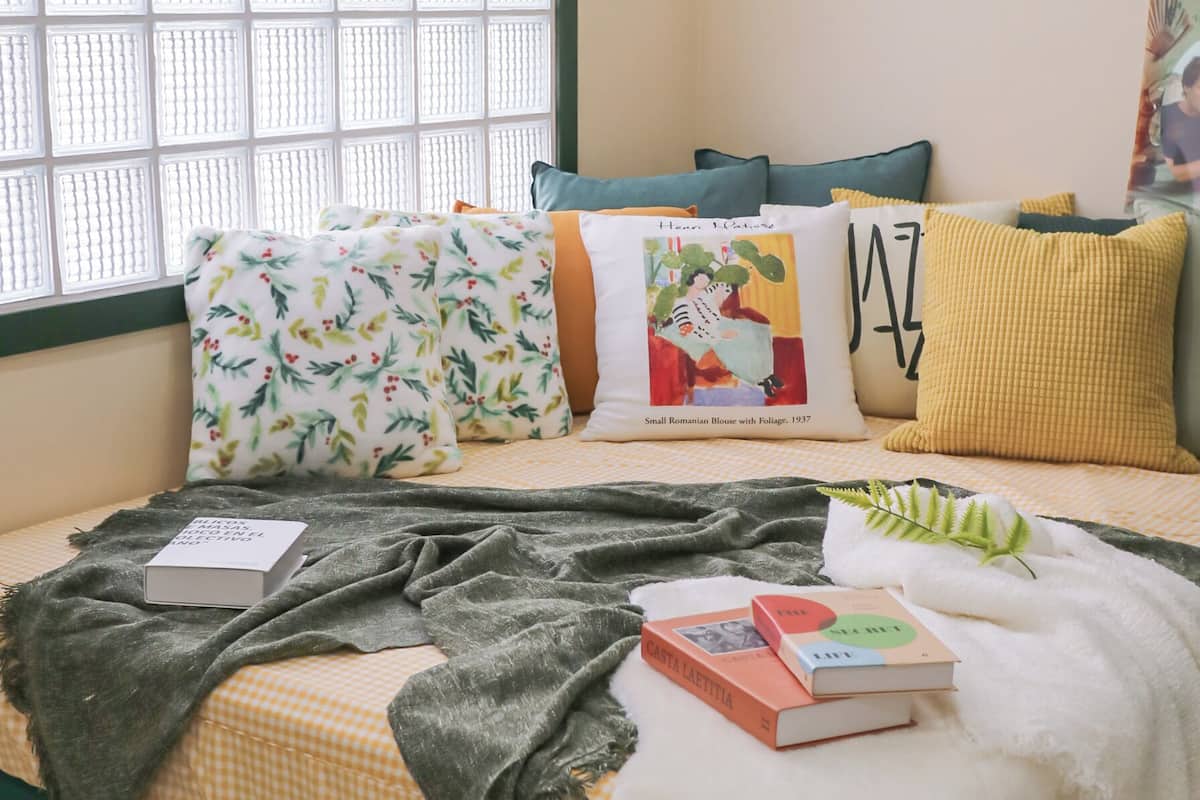 A cozy reading nook with a checkered bedspread, a variety of pillows, and a bookshelf with books.