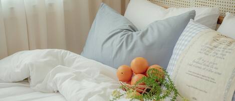 A neatly made bed with white bedding, a basket of oranges, and a decorative pillow.