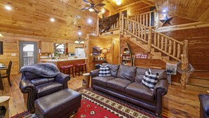 A cabin interior with a wooden interior, a leather sofa, a dining area, and a staircase.