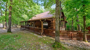 A rustic wooden cabin with a porch, surrounded by trees.