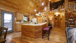 A wooden cabin interior with a kitchen, dining area, and a loft bedroom.