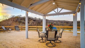 A covered outdoor patio with a wooden deck, a table with chairs, string lights, and a view of a natural landscape. - Remote private fishing getaway! (Chico)