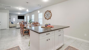 A modern kitchen with white cabinetry, a central island, and a dining area with wooden chairs. - Remote private fishing getaway! (Chico)