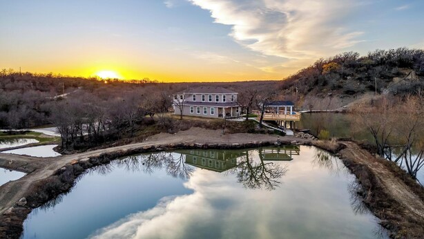 A house with a dock extending into a calm body of water, surrounded by a natural landscape with trees and a clear sky. - Remote private fishing getaway! (Chico)