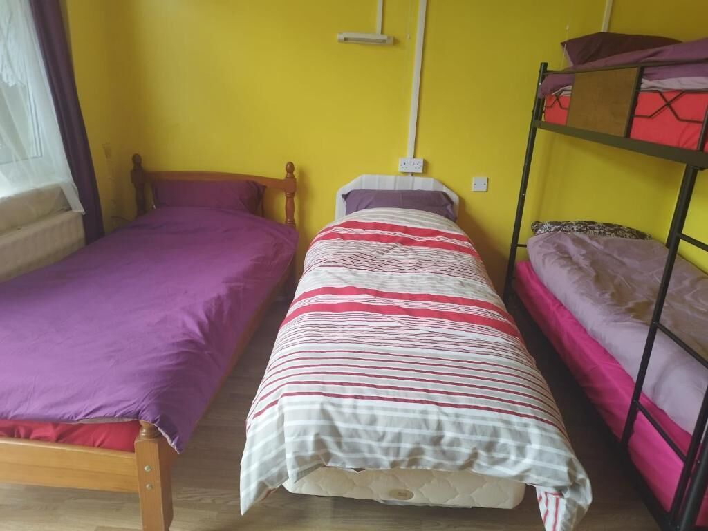 A room with two single beds, a bunk bed, wooden flooring, and a window with curtains.