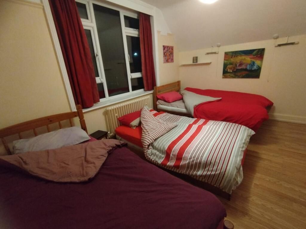 A bedroom with two beds, a window with red curtains, a radiator, and a painting on the wall.