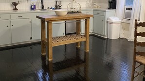 A kitchen with white cabinets, a wooden table, and a window with curtains. - Charming 3-bedroom country cottage on a 
Small  pond (Bellville)