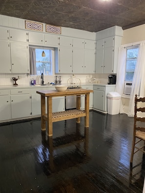 A kitchen with white cabinets, a wooden table, and a window with curtains.