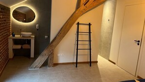 Une pièce avec un escalier en bois, un miroir rond, un lavabo et une échelle.