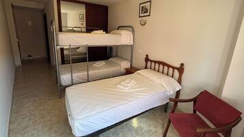Ein Zimmer mit zwei Etagenbetten, einem Einzelbett, einem Sessel und einem Spiegel.