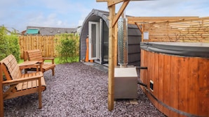 Una terraza de madera con jacuzzi, una parrilla y un área de estar techada al aire libre.