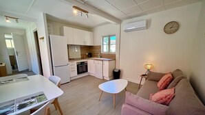 A modern kitchen with white cabinets, a dining area with a white table and chairs, and a living area with a pink sofa and a lamp.